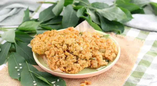 Fiori di sambuco fritti dorati e croccanti su un piatto, con foglie verdi e piccoli fiori di sambuco tutt'intorno.