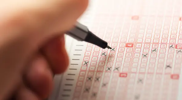 Ręka z długopisem zaznacza liczby na kuponie lotto, marząc o wygranej w jackpot.