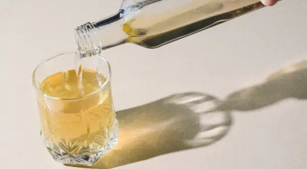 Klarer Flüssigkeit wird aus einer Glasflasche in ein Glas gegossen. Ein gesunder Schluck Essigwasser für den Tag.