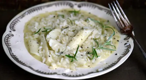 Krämig risotto med sparris och rosmarin, perfekt för ett svamprisotto recept. Serveras på en vacker tallrik med en gaffel.