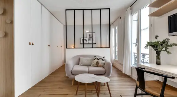 Ein moderner Raumteiler mit schwarzen Metallstreben trennt den Wohnbereich mit einem Sofa und Couchtisch vom Rest des Zimmers.