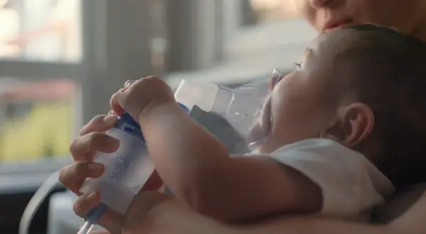 Mama pomaga maluszkowi z mokrym kaszlem u niemowlaka, stosując inhalator.