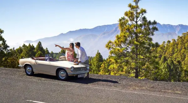 Pareja planeando sus rutas en coche por La Palma, con un descapotable y un paisaje montañoso de pinos.