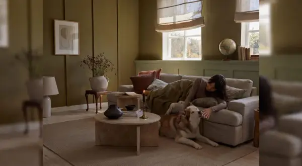 Gemütliches Wohnzimmer in warmen Farben. Eine Frau kuschelt mit ihrem Hund auf dem Sofa, umgeben von erdigen Tönen und sanftem Licht.