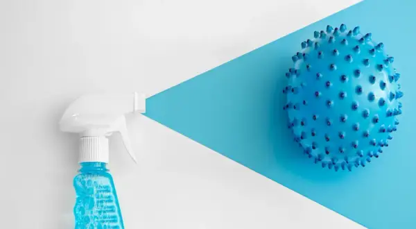 Botella rociadora con líquido azul y burbujas, apuntando a una esfera azul con púas. Considerar clorhexidina contraindicaciones.