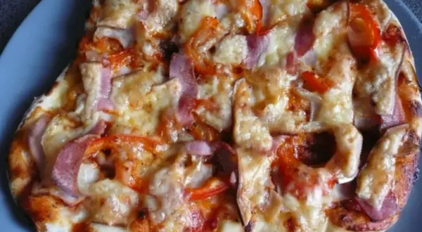 Pyszna pizza z szynką, papryką i cebulą, zapieczona pod ciągnącym się serem. Idealna na szybki obiad.