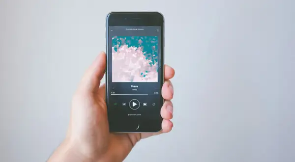 A hand holds a smartphone displaying the Spotify app, showing the song "Peace" by ramp. This image illustrates how to get music on Spotify.