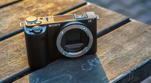 Czarny aparat Sony Alpha ZV-E10 bez obiektywu leży na drewnianym stole.