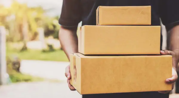 Kurier firmy kurierskiej FedEx niesie trzy paczki.