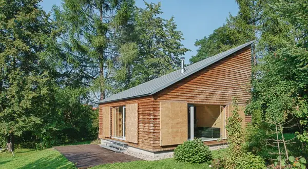 Nowoczesny dom letniskowy z drewnianą elewacją i dużymi przeszkleniami, otoczony zielenią.
