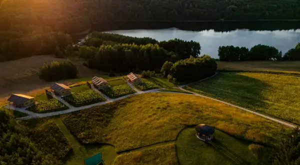 Idealny weekend w Polsce: domki glampingowe nad jeziorem, otoczone zielenią i polami. Słońce zachodzi, rzucając złote światło na krajobraz.