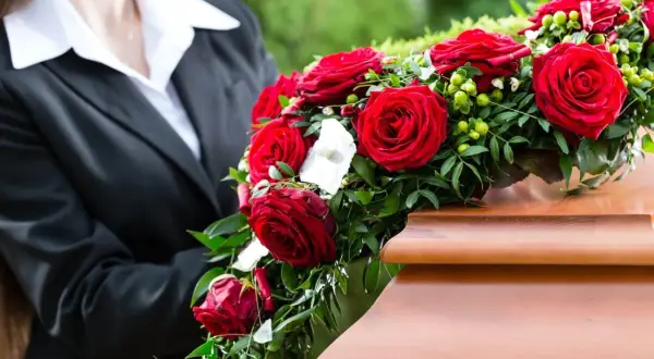 Osoba w czerni kładzie wieniec pogrzebowy z czerwonych róż na trumnie. Wieniec pogrzebowy znaczenie to symbol miłości i pamięci.