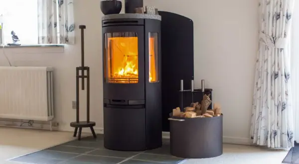 Ein moderner schwarzer Kamin mit brennendem Feuer. Daneben ein Korb mit Holzscheiten, bereit für den Kamin zug.