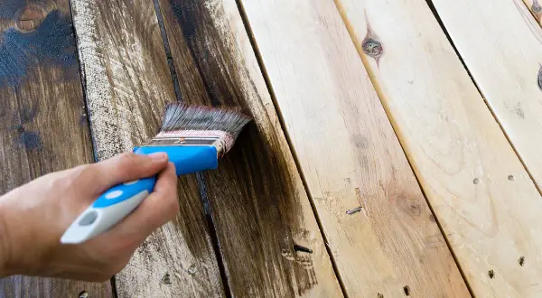 Mano che applica impregnante su assi di legno, recuperando un vecchio tavolo rovinato dalle intemperie.
