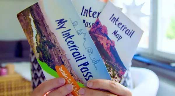 Ręce trzymają broszurę "My Interrail Pass" i mapę. To świetny sposób na podróżowanie po Europie, jeśli zastanawiasz się interrail co to.