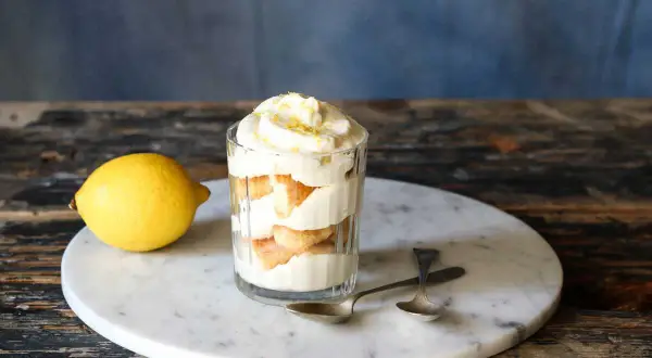 Un délicieux tiramisu aux agrumes, servi dans un verre, avec un citron frais à côté.