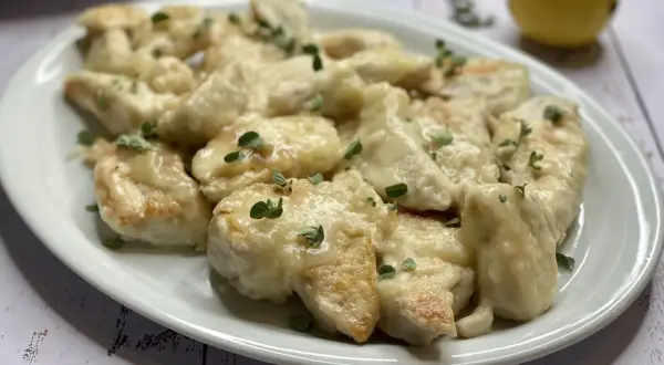 Delizioso pollo al limone ricetta, servito su un piatto bianco con erbe aromatiche e un limone sullo sfondo.