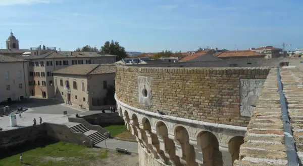 Vista panoramica di Senigallia, Ancona, con un'antica fortezza in primo piano e tetti di tegole rosse sullo sfondo sotto un cielo azzurro.