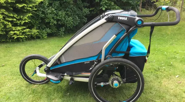 En Thule Chariot Sport 2 barnvagn står på en gräsmatta. Den är blå och svart med stora hjul.