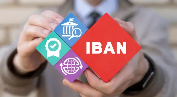 Ręce trzymają puzzle z napisem IBAN i ikonami: bank, pieczęć jakości, globalny zasięg.