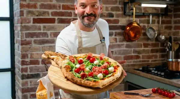 Ein Mann präsentiert stolz eine köstliche Pizza mit Rucola, Kirschtomaten und Mozzarella. Perfekt für einen gemütlichen Pizza Abend!