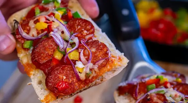 Pyszna zapiekanka z chorizo, papryką i cebulą, trzymana w dłoni.