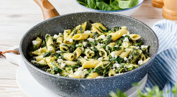 Penne-Nudeln mit Spinat und zerbröseltem Feta in einer Pfanne.