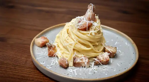 Pyszne spaghetti carbonara z chrupiącym guanciale, posypane parmezanem i świeżo mielonym pieprzem.