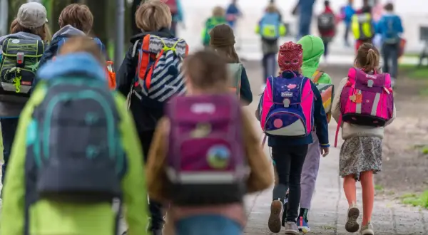 Kinder mit bunten Schulranzen gehen gemeinsam auf dem Weg zur Grundschule. Ein sicherer Schulweg ist wichtig für alle.