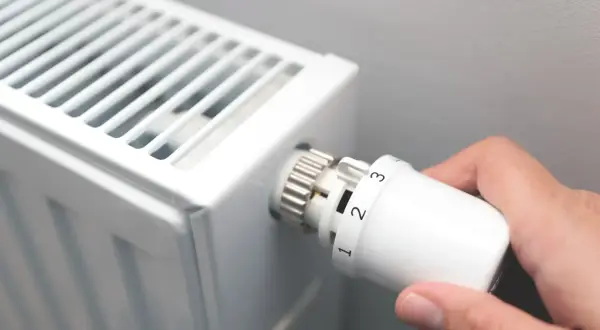 Dłoń kręci termostatem grzejnika, ustawiając temperaturę. Czas zacząć sezon grzewczy.