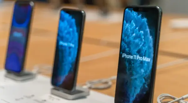 Trois iPhone 11 Pro Max sont alignés sur un présentoir, affichant un fond d'écran bleu abstrait.