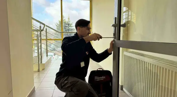 Mężczyzna próbuje otworzyć drzwi bez klucza, używając śrubokręta. Obok niego stoi torba z narzędziami.