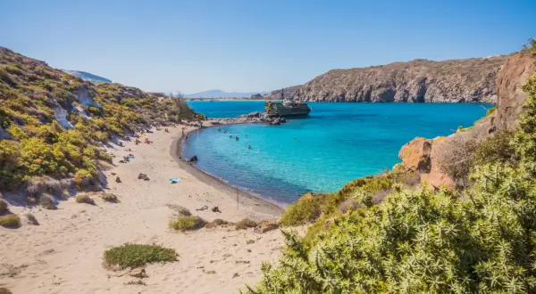 Piękna plaża na wyspie Nisyros z turkusową wodą, łodzią i ludźmi odpoczywającymi na piasku.