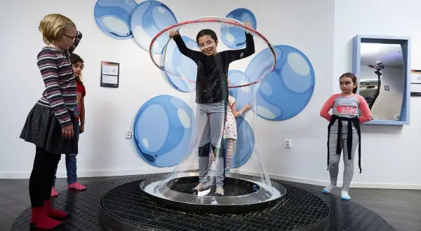Barn utforskar vetenskap på 2047 science center, en flicka är innesluten i en gigantisk såpbubbla.