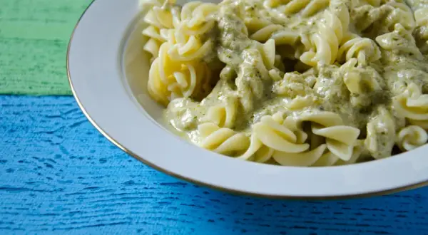Fusilli-Nudeln in cremiger Pesto Sahne Sauce, serviert auf einem bunten Holztisch.