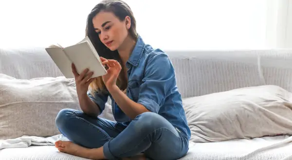 Odkryj sekrety domowych bibliotek gwiazd! Co naprawdę czytają znani i lubiani? Młoda kobieta w dżinsowej koszuli zanurzona w lekturze na kanapie.