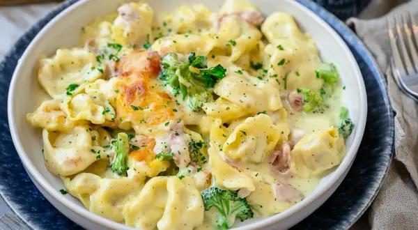 Cremiger Tortellini Auflauf mit Brokkoli und Schinken, überbacken mit Käse und bestreut mit Petersilie. Ein köstliches Gericht!