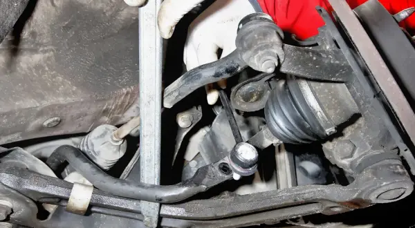 Montaż łącznika stabilizatora Toyota Yaris 1. Widoczna ręka w rękawiczce przykręca element zawieszenia.