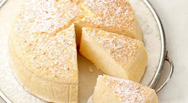 Ein luftiger, fluffiger japanischer Cheesecake, bestäubt mit Puderzucker, auf einer Servierplatte.