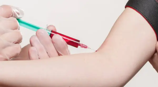 Prélèvement sanguin : une seringue verte et rouge est insérée dans un bras.