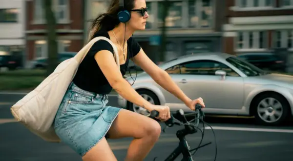 Frau fährt Fahrrad mit Kopfhörern und Tasche. Ob man mit AirPods Fahrrad fahren darf, ist eine Frage der Sicherheit und des Gehörs.