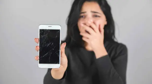 Zrozpaczona kobieta pokazuje pęknięty, czarny ekran w telefonie.