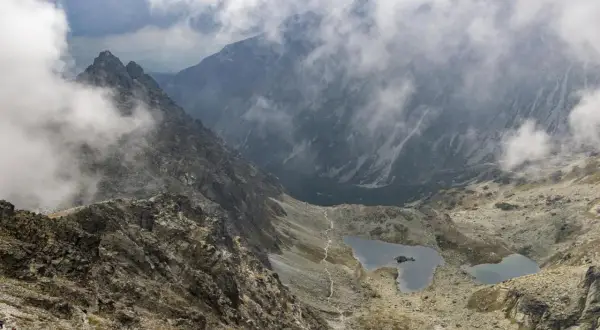 Widok na Tatry z mgłą, idealne miejsce na pierwsze górskie wędrówki. Szlak prowadzi w dół do malowniczych jezior.