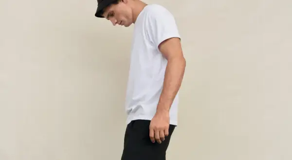 Młody mężczyzna w czarnym kapeluszu typu bucket hat i białej koszulce, spodnie w stylu skate.