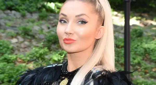 Cleo, której wiek dodaje jej uroku, w czarnej, ozdobnej kreacji z piórami.