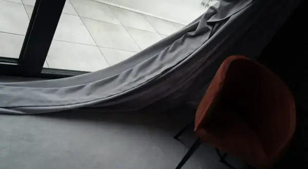 Szare zasłony swobodnie opadają na podłogę, tworząc przytulną atmosferę wokół pomarańczowego fotela.