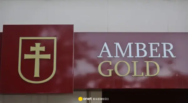 Złoty symbol krzyża na bordowym tle obok napisu AMBER GOLD.