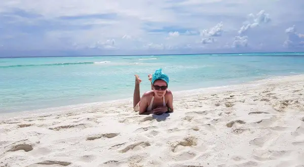 Wrzesień na Malediwach to idealna pogoda na plażowanie. Kobieta w turkusowym turbanie leży na białym piasku, ciesząc się słońcem i błękitem oceanu.