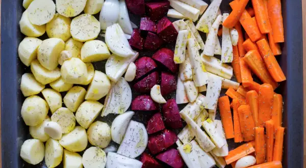 Ugnsrostade rotfrukter: potatis, morötter, palsternacka, rödbetor och lök, kryddade och redo för ugnen.