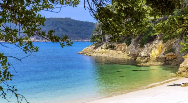 Playa caolín, una cala virgen de arena blanca y aguas turquesas, rodeada de acantilados y vegetación frondosa.